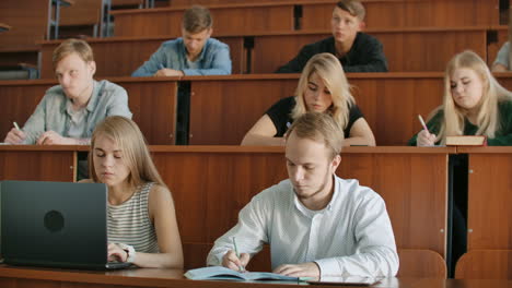 Young-men-and-women-sitting-in-a-university-or-college-classroom-write-a-lecture-with-a-pen-and-using-a-laptop.-Institute-education