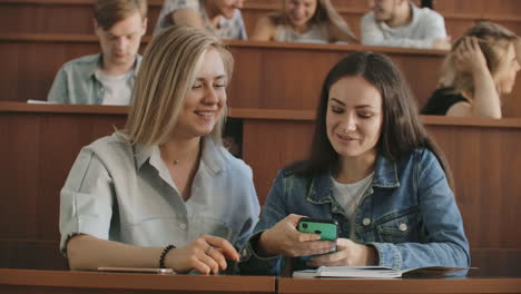 Female-students-with-a-smartphone-in-their-hands-laughing-in-the-audience-during-a-break-for-a-lecture-at-the-University.