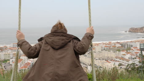 Boy-on-the-swing-against-ocean-and-coast-in-Nazare-Portugal