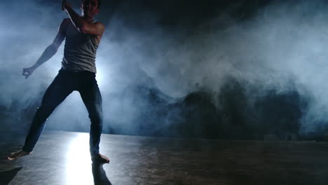 Modern-ballet-a-man-from-a-sitting-position-on-the-stage-jumps-backflip-with-rotation-on-a-dark-stage-in-the-smoke-in-the-spotlight.