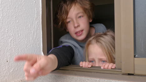 Sister-and-brother-looking-outside-through-the-open-house-window