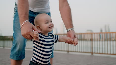 Happy-cute-baby-learns-to-walk-and-takes-first-steps-in-the-city-under-the-control-of-his-grandfather