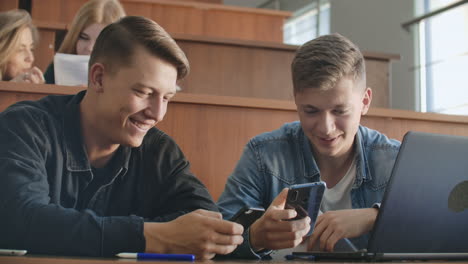 Männliche-Studenten-Mit-Einem-Smartphone-In-Der-Hand-Lachen-Während-Einer-Vorlesungspause-An-Der-Universität-Im-Publikum.