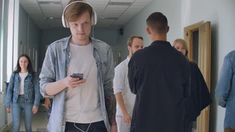 An-introverted-man-walks-in-a-crowd-of-College-students-and-listens-to-music.-Concentrate-on-your-thoughts.-Modern-student-in-white-headphones-in-the-hall-of-the-University