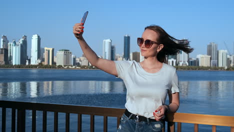 caucasian-woman-is-taking-selfies-by-mobile-phone-outdoors-in-Dubai-Marina-in-sunny-day.