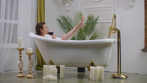 Relax-lying-in-a-white-bath-with-a-glass-of-red-wine.-Young-woman-relaxing-in-hot-relaxing-bath.