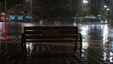 Empty-bench-and-road-traffic-in-the-city-at-rainy-night