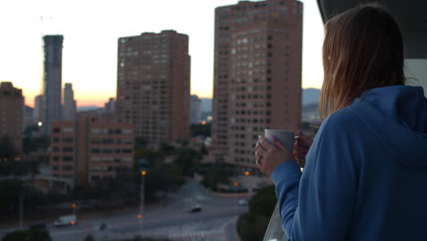 Woman-having-coffee-and-looking-at-city-in-early-morning