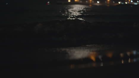 Dunkle-Meereswellen-Waschen-Das-Ufer-Mit-Lichtreflexion-In-Der-Nacht