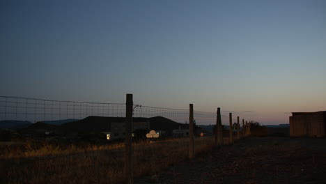 Car-on-the-country-road-with-wire-metal-fence-alongside-dusk-view