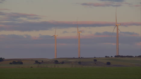 Drei-Elektrische-Windkraftanlagen-Bei-Sonnenuntergang-Auf-Einem-Feld