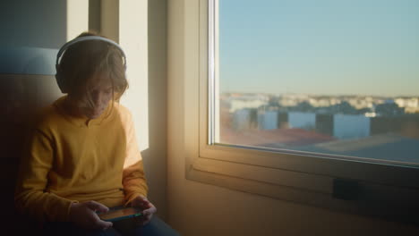 Teenage-Boy-Playing-Game-on-Phone-at-Dawn-by-Window