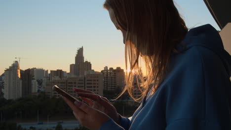 Urban-woman-checking-messages-on-the-phone-view-against-city-at-sunrise