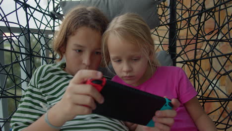 Geschwister-Spielen-Videospiele-Auf-Einem-Schaukelstuhl-Auf-Dem-Balkon