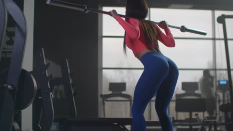 The-girl-slowly-crouches-with-a-barbell-on-her-shoulders.-She-pumps-the-muscles-of-the-buttocks.