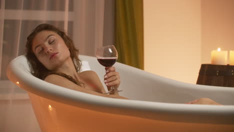 A-young-beautiful-Caucasian-brunette-lies-in-the-bathroom-by-candlelight-in-a-pleasant-evening-atmosphere-resting-from-stress-and-relaxing-drinking-red-wine-from-a-glass