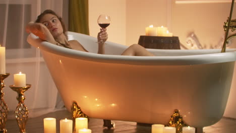 Frau-Liegt-Im-Schaumbad-Im-Licht-Der-Kerzen,-Um-Sich-Zu-Entspannen-Und-Wein-Zu-Trinken.-Romantische,-Entspannende-Aromatherapie-Atmosphäre.-Badezimmer-Mit-Kerzen.