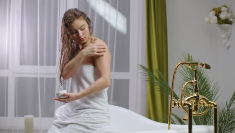 Beauty-and-body-care-female-elbow-pain-and-health-care-concept.-slow-motion-of-caucasian-woman-applying-lotion-cream-moisturizer-relaxing-in-bed-in-white-cozy-apartment-near-window.-hand-touching-careful