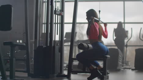 A-young-girl-with-pumped-buttocks-and-a-slim-body-does-an-exercise-on-the-back-muscles-on-a-special-training-machine.-She-uses-extra-load-for-better-results.