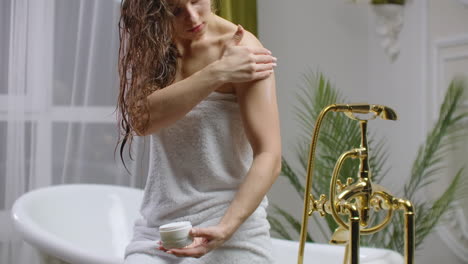 Beauty-and-body-care-female-elbow-pain-and-health-care-concept.-slow-motion-of-caucasian-woman-applying-lotion-cream-moisturizer-relaxing-in-bed-in-white-cozy-apartment-near-window.-hand-touching-careful