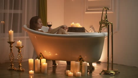 Woman-bathing-with-pleasure-lying-down-in-the-tub-with-foam-and-drinking-red-wine-spending-time-in-luxury-spa-resort