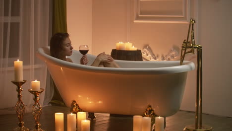 Frau-Liegt-Im-Schaumbad-Im-Licht-Der-Kerzen,-Um-Sich-Zu-Entspannen-Und-Wein-Zu-Trinken.-Romantische,-Entspannende-Aromatherapie-Atmosphäre.-Badezimmer-Mit-Kerzen.