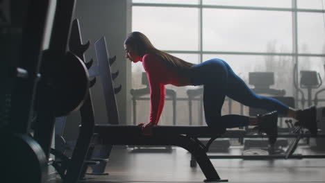 The-girl-in-the-blue-leggins-and-short-pink-top-is-doing-a-circular-workout-in-the-gym.-She-pumps-the-muscles-of-the-buttocks-and-back-of-the-thigh.