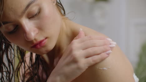 Woman-applying-cream-on-her-skin-in-bathroom-while-siting-on-bath-tub