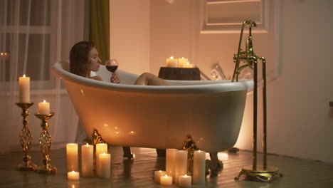 A-young-beautiful-Caucasian-brunette-lies-in-the-bathroom-by-candlelight-in-a-pleasant-evening-atmosphere-resting-from-stress-and-relaxing-drinking-red-wine-from-a-glass