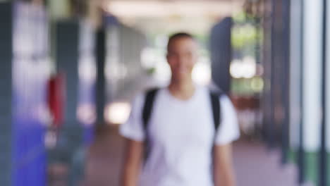 Mixed-race-teenage-boy-walks-into-focus-in-school-corridor