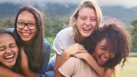 Four-happy-teenage-girls-piggybacking-outdoors,-close-up