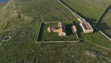 High-angle-bird's-eye-view-orbits-around-old-decrepit-abandoned-military-building-in-Minorca-Spain