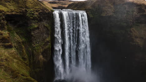 Aerial-view-of-birds-flying-around-the-Skogafoss-waterfall,-autumn-day-in-Iceland---pull-back,-drone-shot