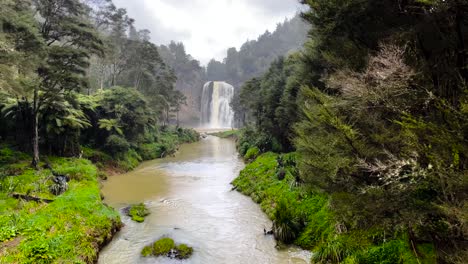 Waterfall-flowing-into-muddy-river-on-rainy-day,-Hunua-Regional-Park,-New-Zealand