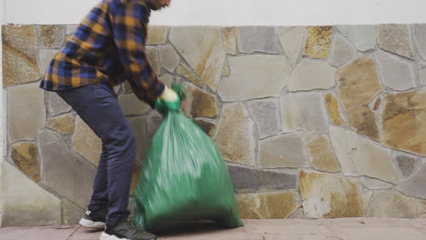 caucasian-male-picking-up-heavy-garbage-trash-bag-filled-with-Biological-Food-Waste,-Recyclable-Bottles-Garbage