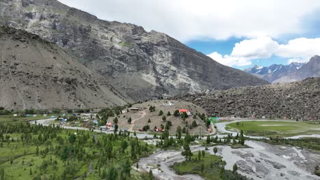 Aerial-drone-rotating-shot-over-village-houses-on-top-of-a-hill-with-Indus-river-flowing-alongside-Basho-Valley,-surrounded-by-mountain-range-in-Skardu,-Pakistan