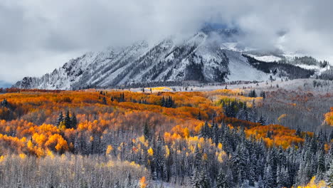 Stunning-Kebler-Pass-Crested-Butte-Colorado-stunning-fall-winter-first-snow-seasons-collide-aerial-cinematic-drone-yellow-aspen-tree-forest-Rocky-Mountains-fog-clouds-lifting-upward-jib-motion