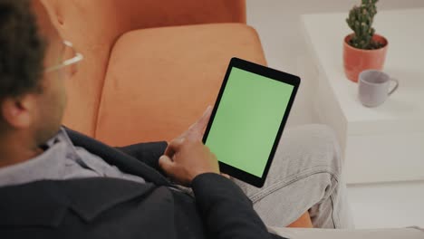 Mann-Auf-Sofa-Mit-Tablet,-Zoomt-Und-Tippt-Auf-Den-Grünen-Bildschirm,-Schaut-Zu-Und-Nickt