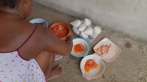 Ghanaian-woman-cooking,-serving-stew-and-fish-on-a-plate-accompanied-by-banku,-typical-Ghanaian-dumpling