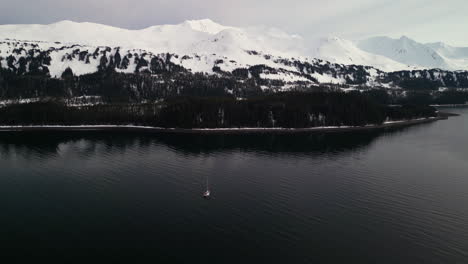 Drone-shot-of-a-sailboat-in-front-of-snowy-mountains-of-Montague-Island,-Alaska