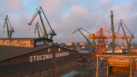 Aerial-view-of-drone-flying-above-shipyard-in-Gdansk-at-the-sunset-with-cranes-in-the-background