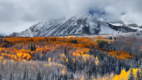 Dramatic-Kebler-Pass-Crested-Butte-Colorado-stunning-fall-winter-first-snow-seasons-collide-aerial-cinematic-drone-yellow-aspen-tree-forest-Rocky-Mountains-fog-clouds-lifting-upward-jib-motion