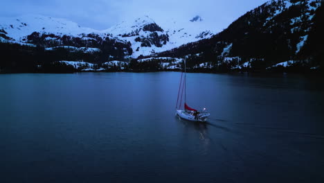 Drone-following-a-sailing-boat-moving-in-middle-of-snowy-peaks,-in-gloomy-Alaska