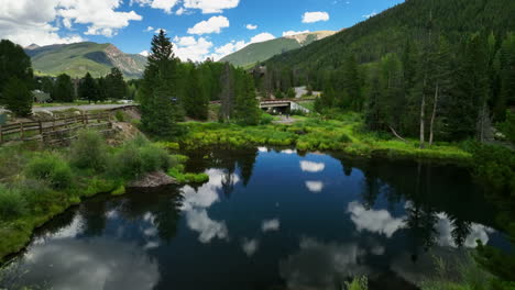 Pond-lake-mirror-reflection-clouds-aerial-cinematic-drone-Keystone-Blue-River-ski-resort-summer-Breckenridge-Colorado-Vail-resort-Epic-Pass-ski-snowboard-bike-biking-biker-path-slowly-forward-motion