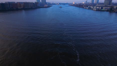 Revealing-Aerial-Shot-over-North-Sea-Canal-in-Amsterdam-with-a-Tanker-Ship-coming,-Twilight