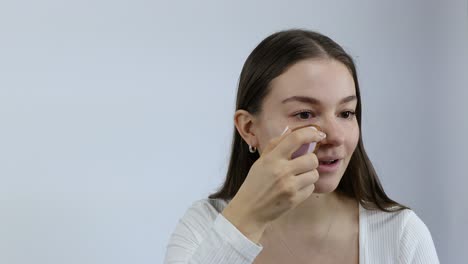 Mujer-Joven-Caucásica-Europea-Aplicando-Base-De-Maquillaje-Con-Esponja-Aislada-Sobre-Fondo-Gris