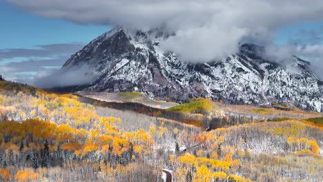 Kebler-Pass-aerial-cinematic-drone-Crested-Butte-Gunnison-Colorado-seasons-collide-early-fall-aspen-tree-red-yellow-orange-forest-winter-first-snow-powder-Rocky-Mountain-peak-dirt-road-backward-motion
