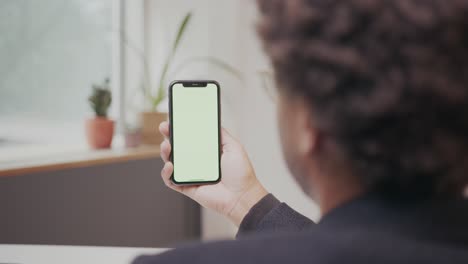Black-man-at-home-office-is-holding-phone,-tapping-and-swiping-on-green-screen