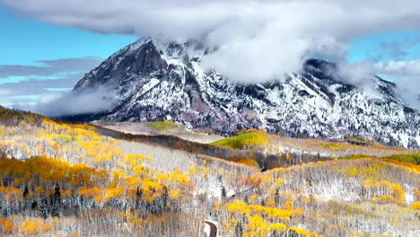 Kebler-Pass-aerial-cinematic-drone-Crested-Butte-Gunnison-Colorado-seasons-collide-early-fall-aspen-tree-red-yellow-orange-forest-winter-first-snow-powder-Rocky-Mountain-peak-dirt-road-forward-motion