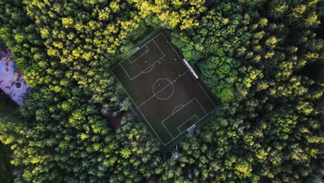 Drone-shot-over-a-soccer-field-in-middle-of-sunlit-woodlands,-summer-evening